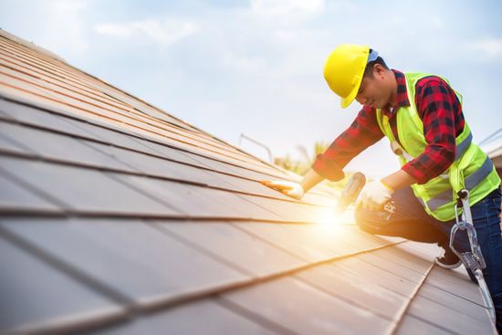 ACE employee nailing shingles onto a roof with the sun rising in the background while wearing all the appropriate safety gear.