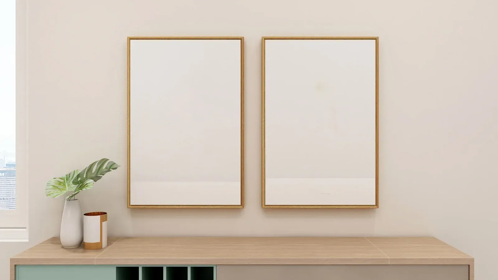Two framed blank posters above a wooden cabinet. A vase with green leaves and decorative items sit on the cabinet.