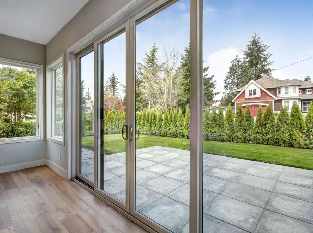Interior view of a room with large glass sliding doors overlooking a patio and a house.