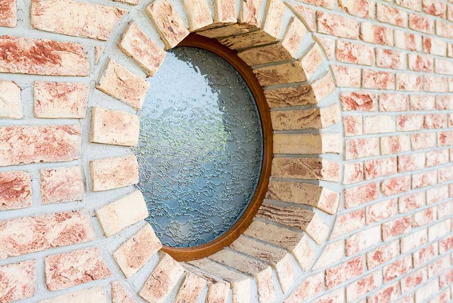 A round window in a brick wall with a wooden frame.