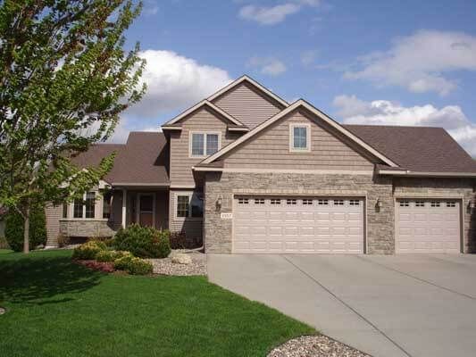 A large house with three garage doors and a tree in front of it
