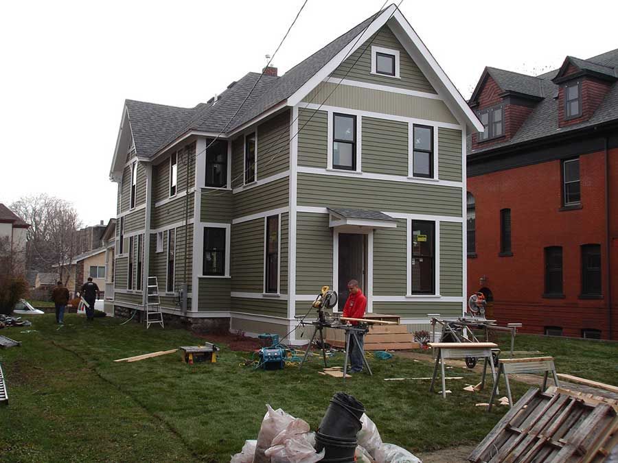 A man in a red jacket is standing in front of a house that is being remodeled.
