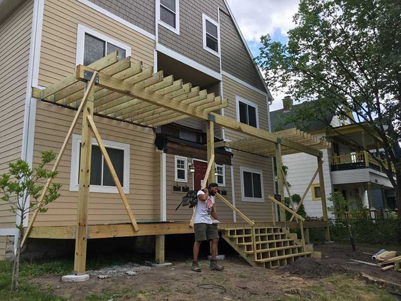A man is standing in front of a house with a wooden deck under construction.