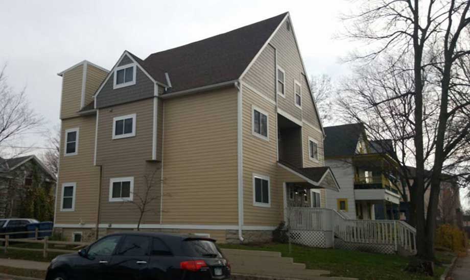 A black car is parked in front of a large house.