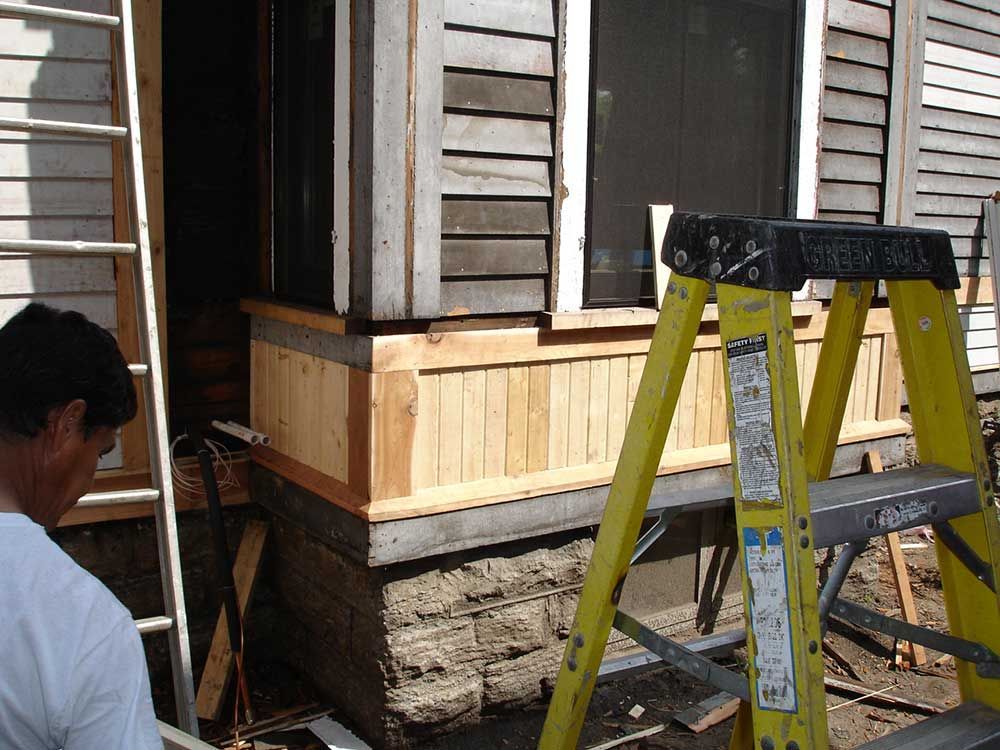 A man is standing next to a yellow ladder in front of a house.