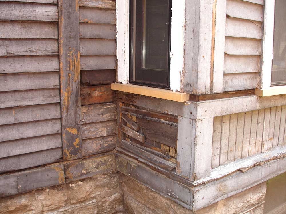 A corner of a building with a window and a broken window sill.