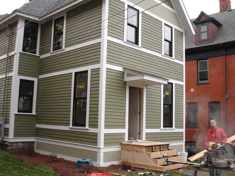 A man is cutting a piece of wood in front of a house