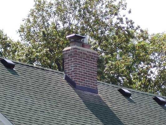 A brick chimney is sitting on top of a green roof.