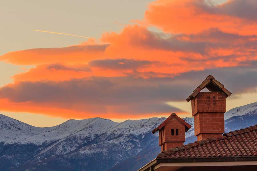 A house with chimneys on the roof and mountains in the background at sunset.