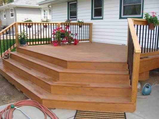 A wooden deck with stairs and a railing in front of a house.