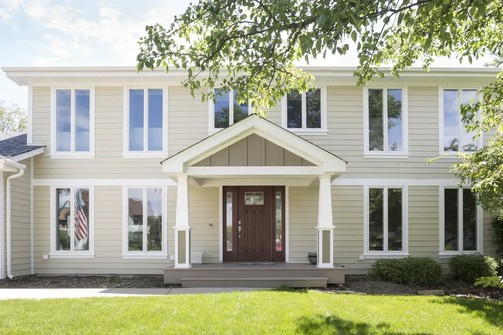 A large house with a porch and a lot of windows is sitting on top of a lush green lawn.