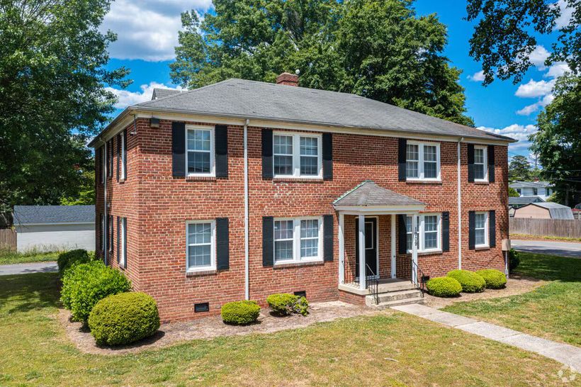 A brick house with black shutters and a gray roof is sitting on top of a lush green lawn.