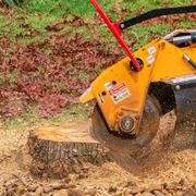 A stump grinder is cutting a tree stump in a yard.