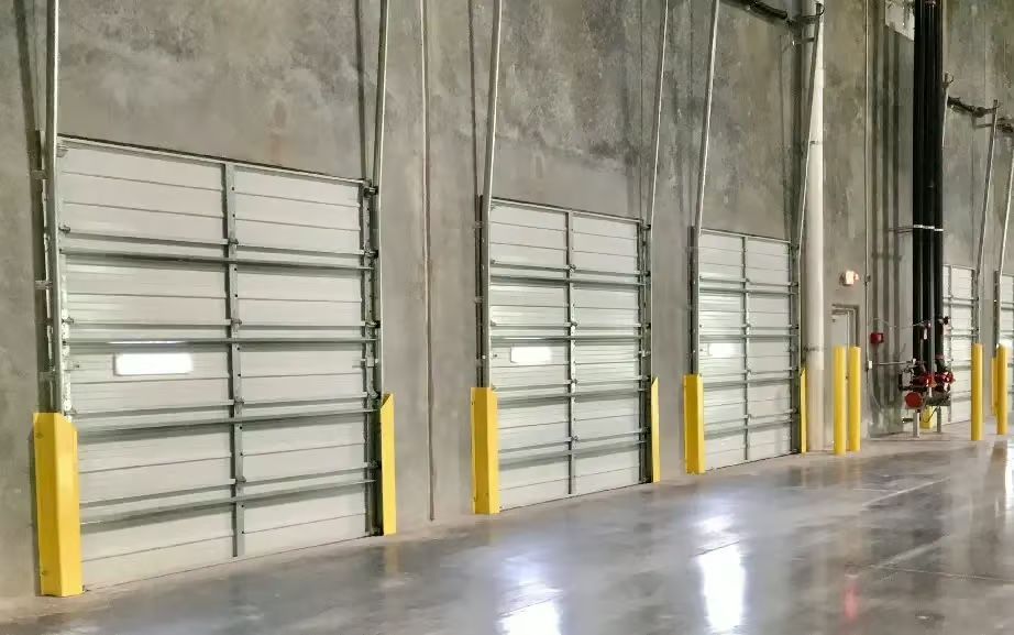 Warehouse interior with loading dock doors, metal frames, yellow bumpers, concrete floor.