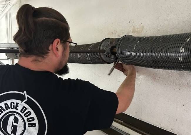 Man fixing garage door spring with tool. Indoors, concrete wall.