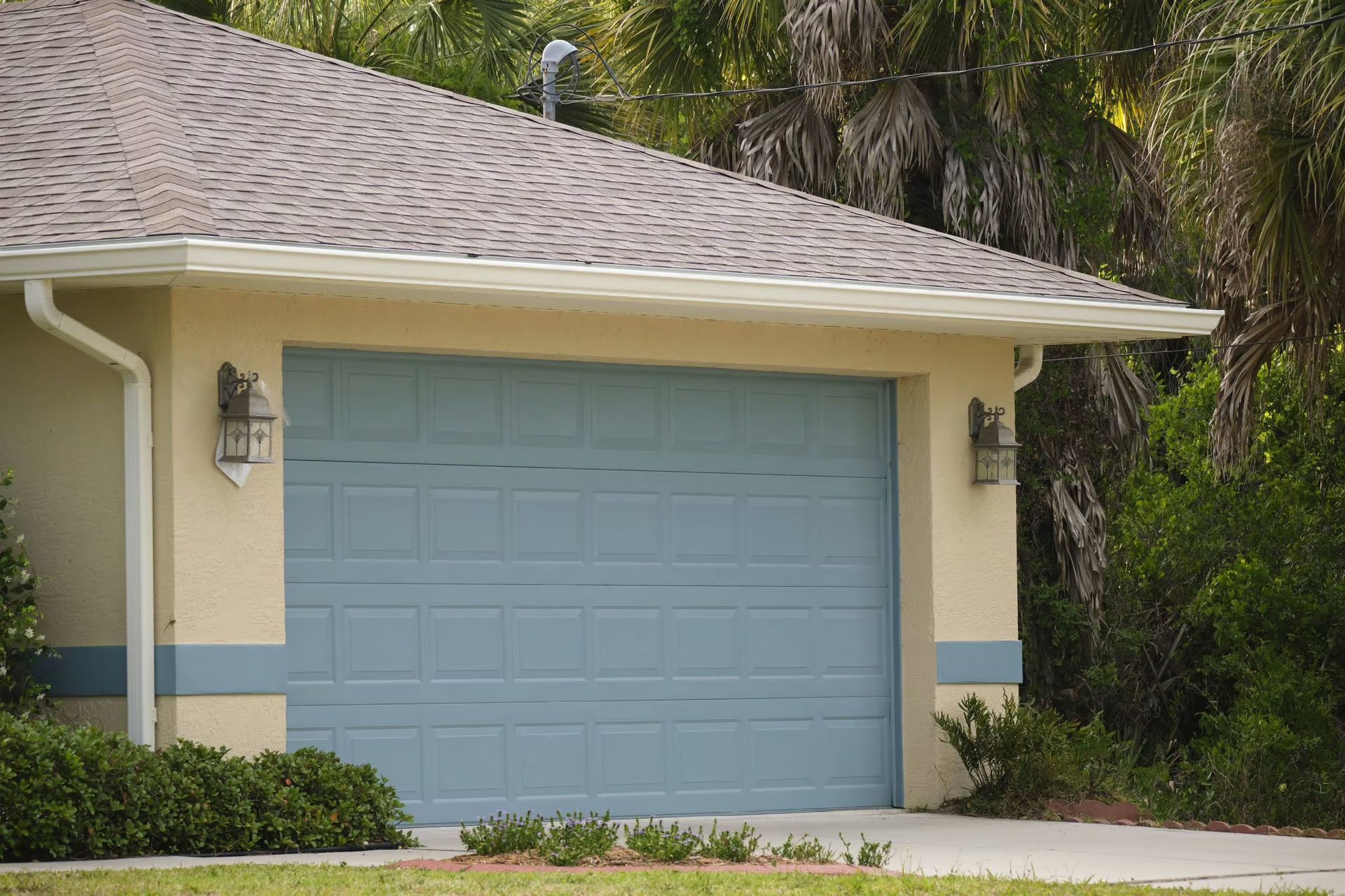 Blue garage door on a beige house with brown roof and green landscaping.