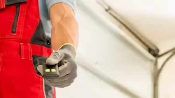 Person in red overalls holding a garage door opener, near an open door.