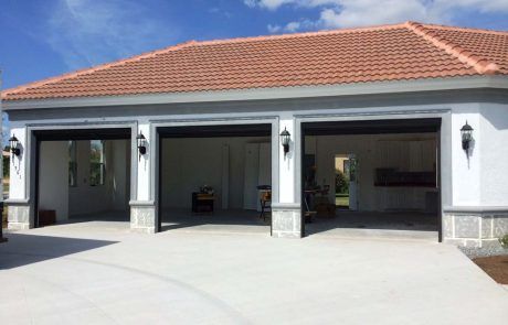 A modern three-car garage with white stucco walls, grey trim, and a tiled roof, open to reveal an interior space.