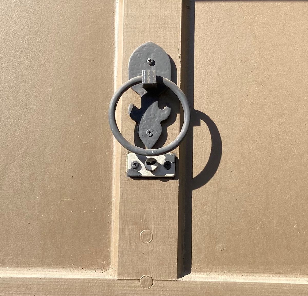 Metal door knocker on a tan door, casting a shadow.