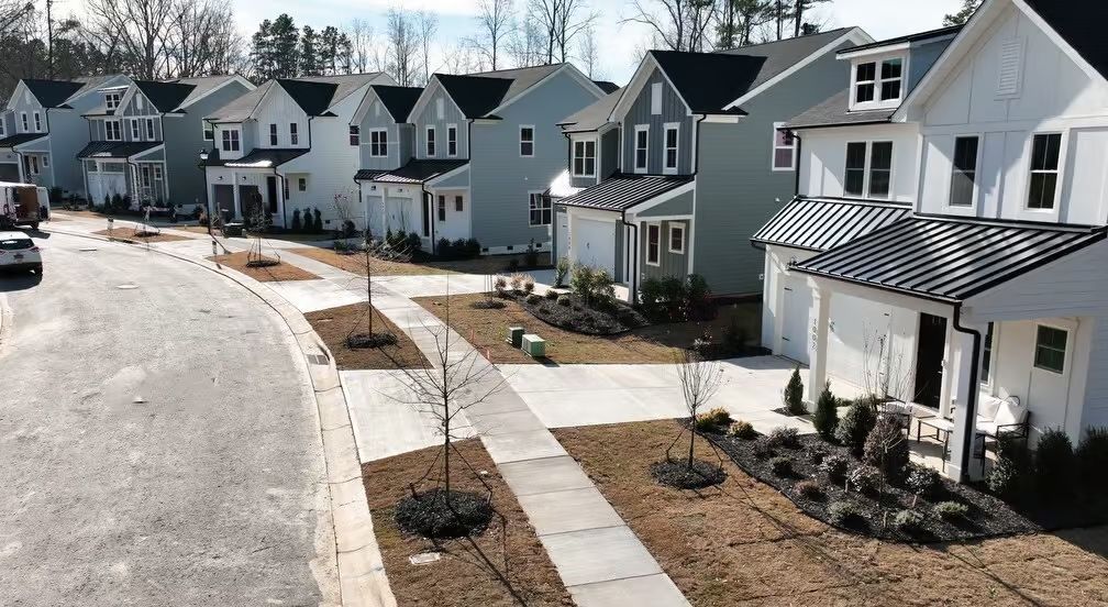 Row of new houses in various colors, along a curved street with sidewalks and young trees.