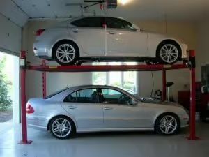 Two silver cars, one atop the other, on a red car lift in a garage.