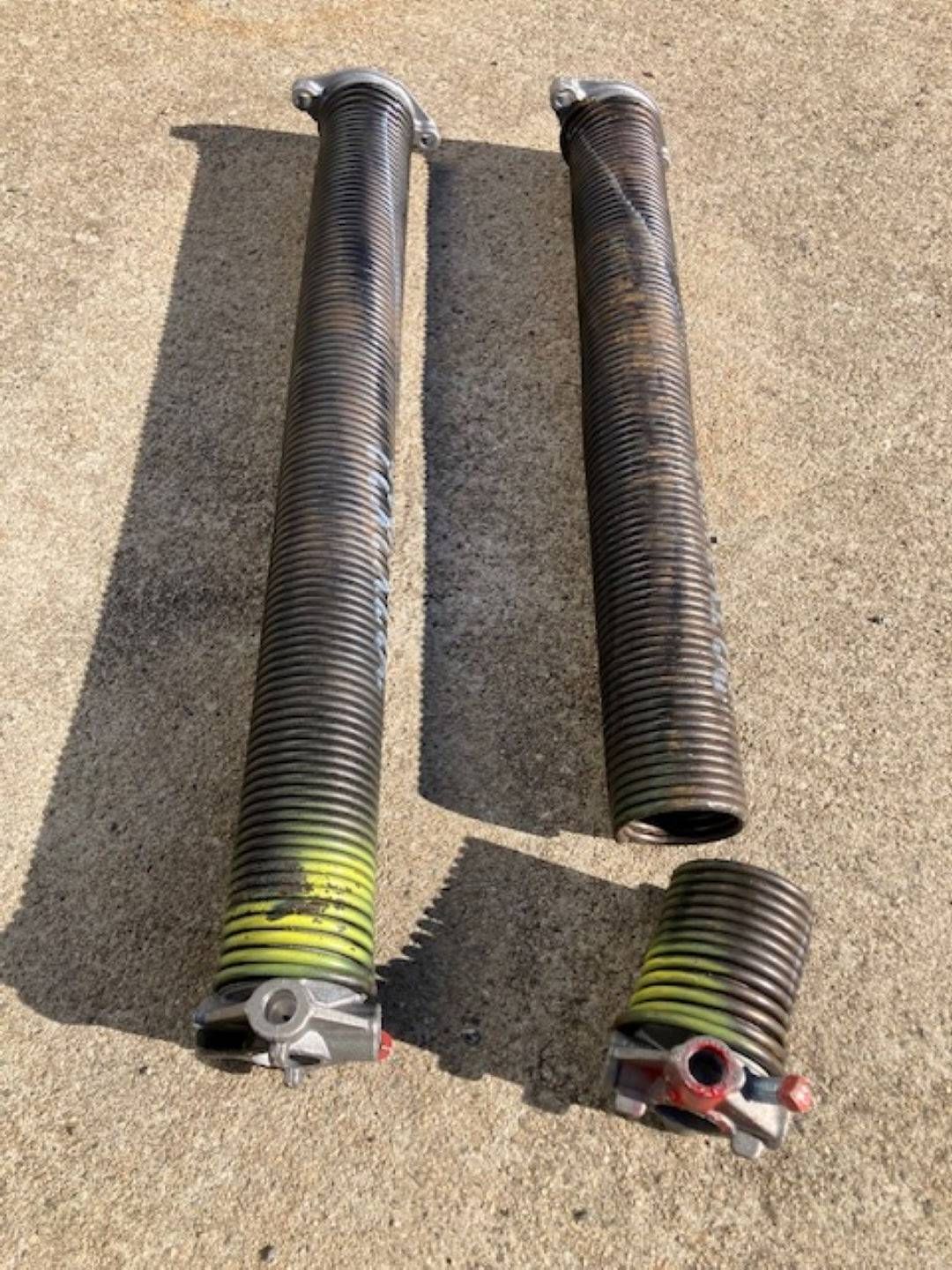 Two broken garage door springs laying on concrete; one in multiple pieces.