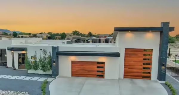 Modern white house with wooden garage doors, against an orange and blue sky.