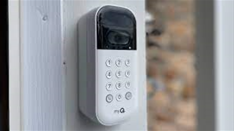 White doorbell camera with keypad mounted on a wooden surface.