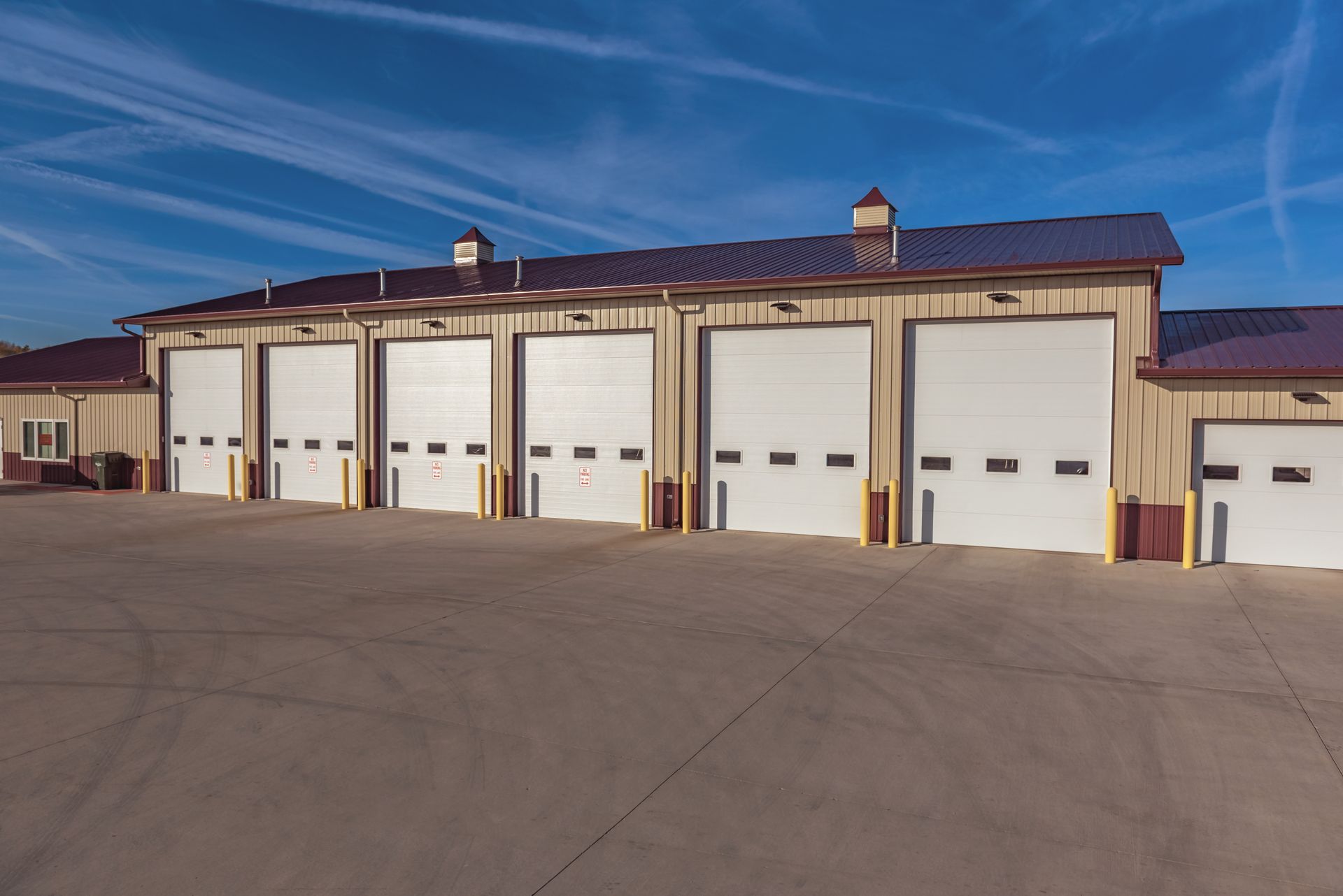 Exterior view of a beige building with multiple white garage doors under a blue sky.