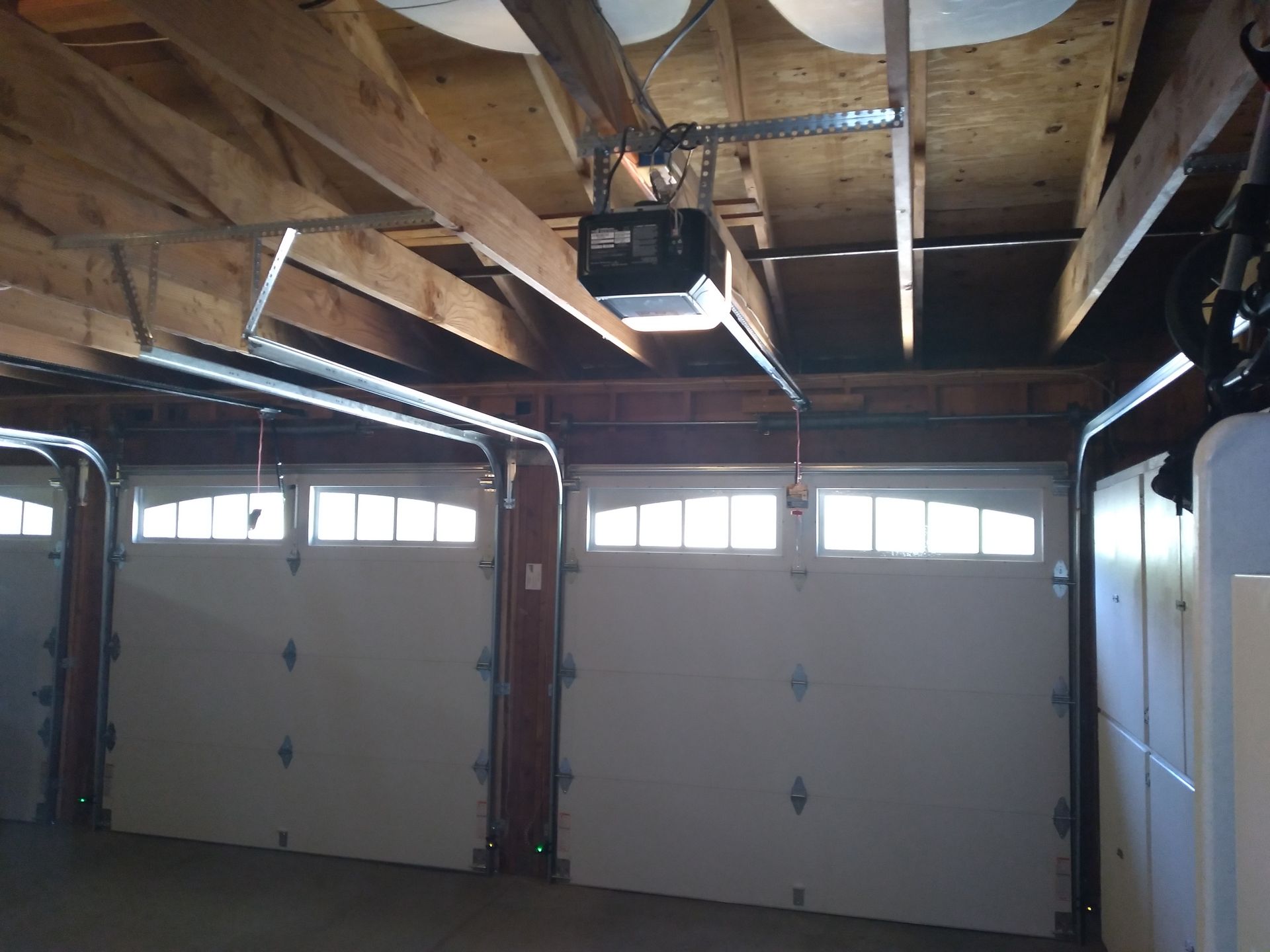 Three white garage doors inside a garage with an automatic opener.