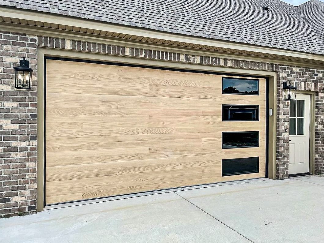 Light wood-toned garage door with black windows on brick home, two black lanterns, and a white door to the right.