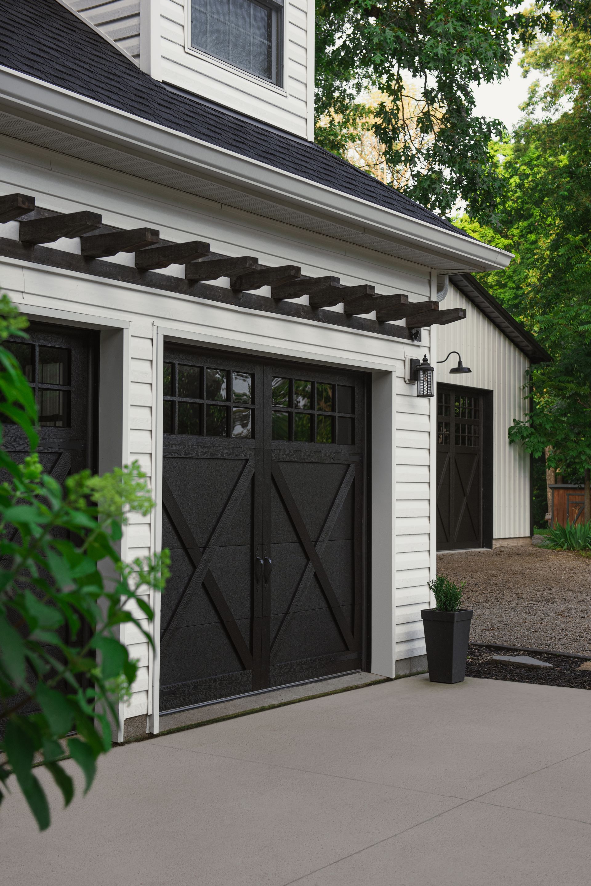 White and black house with black garage doors; a pergola above the doors.