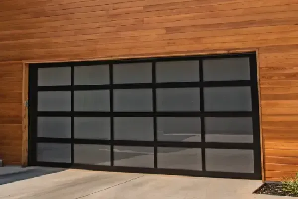 Modern garage door with black frame and frosted glass panels against a wooden exterior.