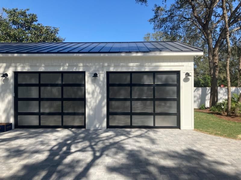 Two modern garage doors with black frames and frosted glass. White stucco building, blue sky.