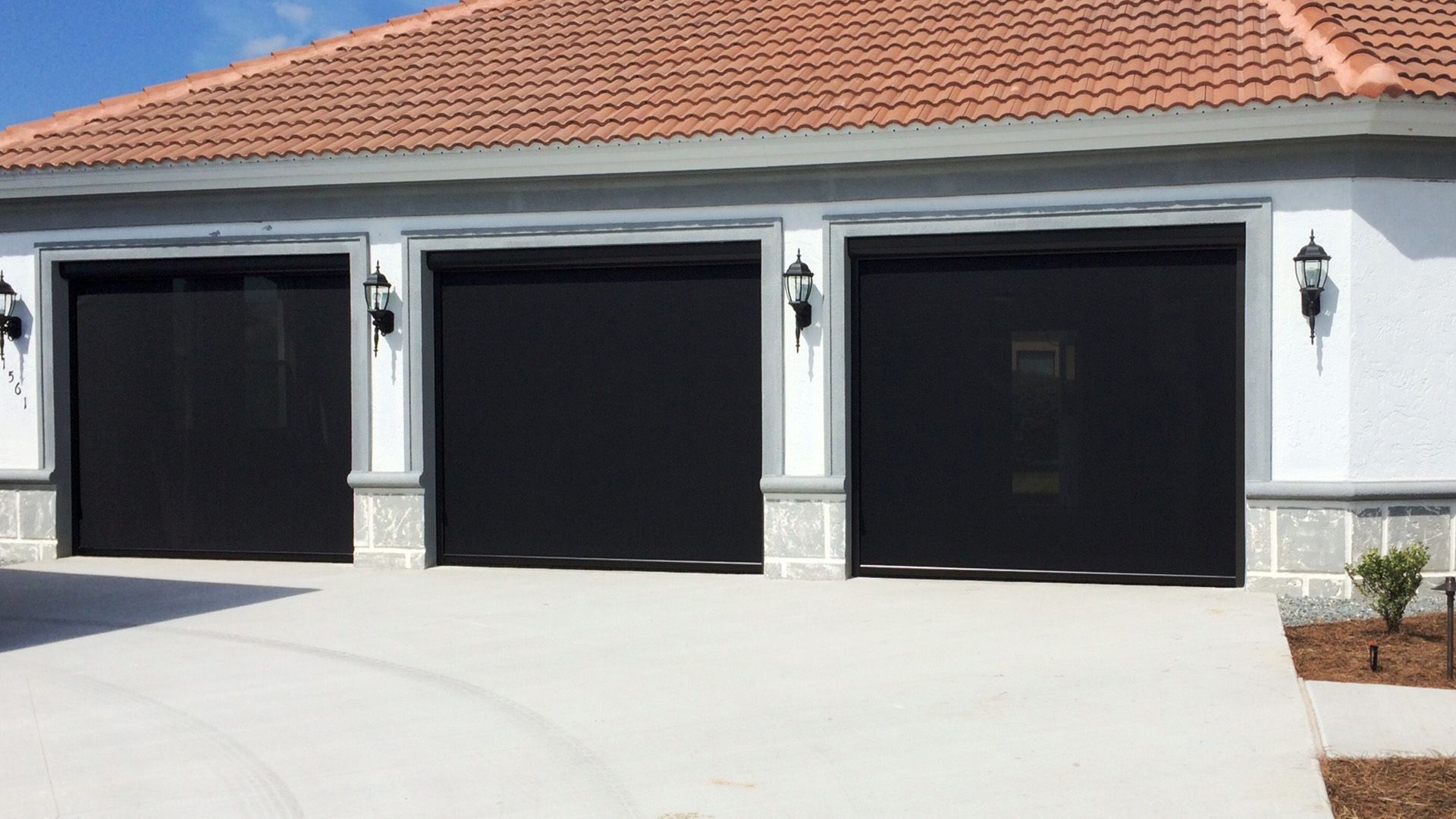 Three garage door openings with black retractable screens installed on a white house with a terracotta tiled roof.