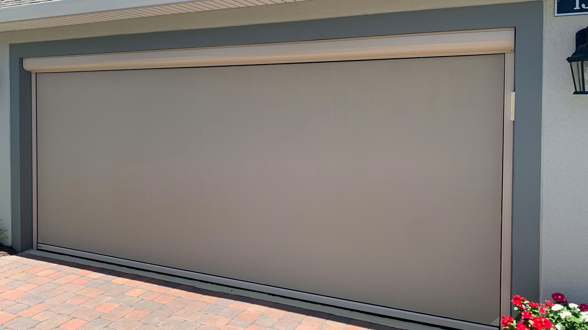 A beige retractable privacy screen covering a garage door opening, framed by dark gray trim on a paved driveway.