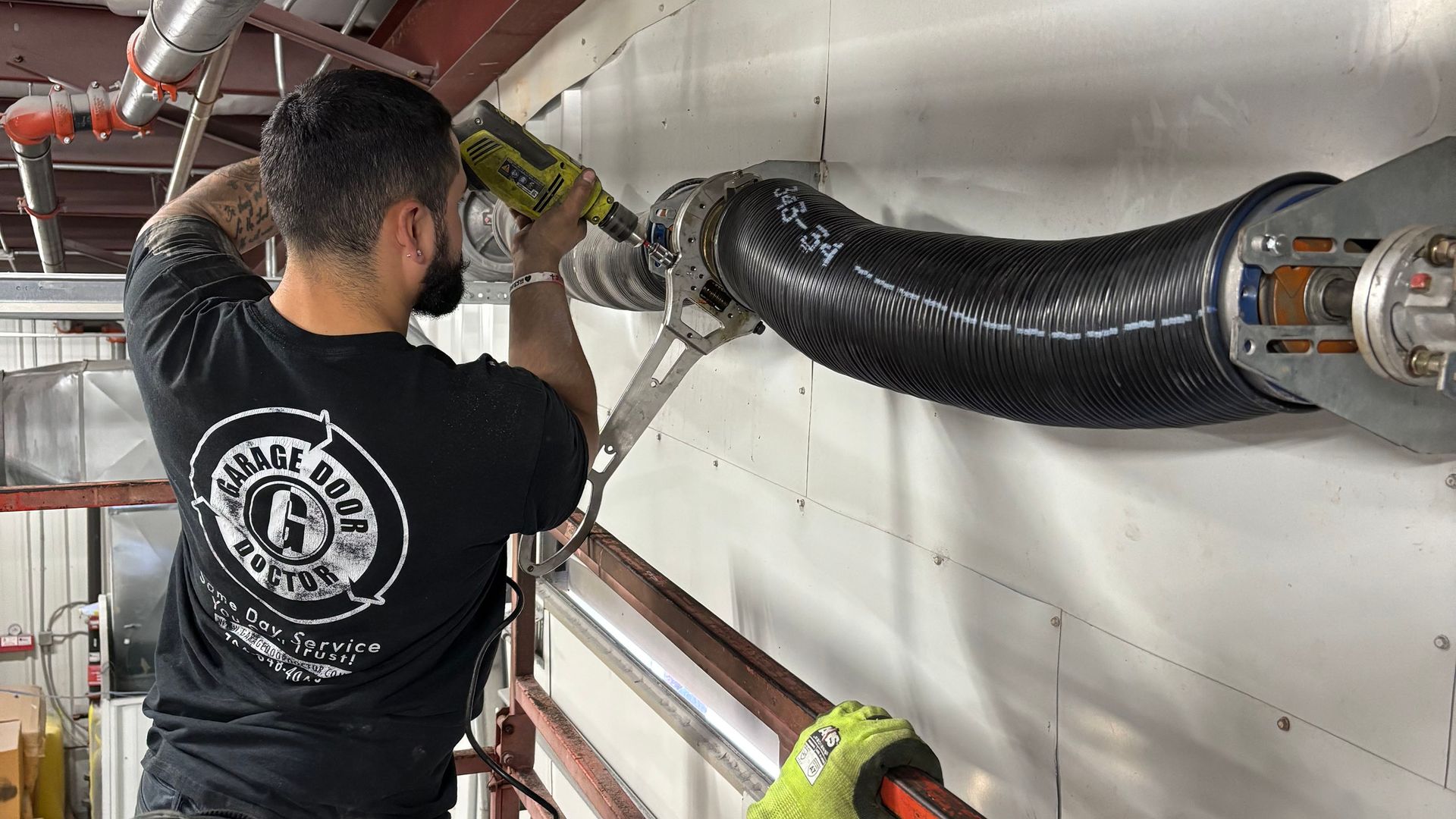 A man wearing a black t-shirt adjusting a garage door spring