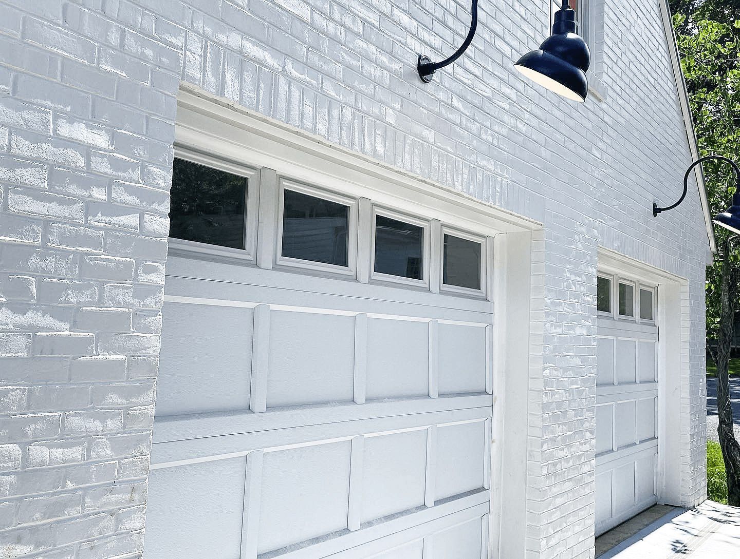 White painted brick garage with two white garage doors and black exterior lights.
