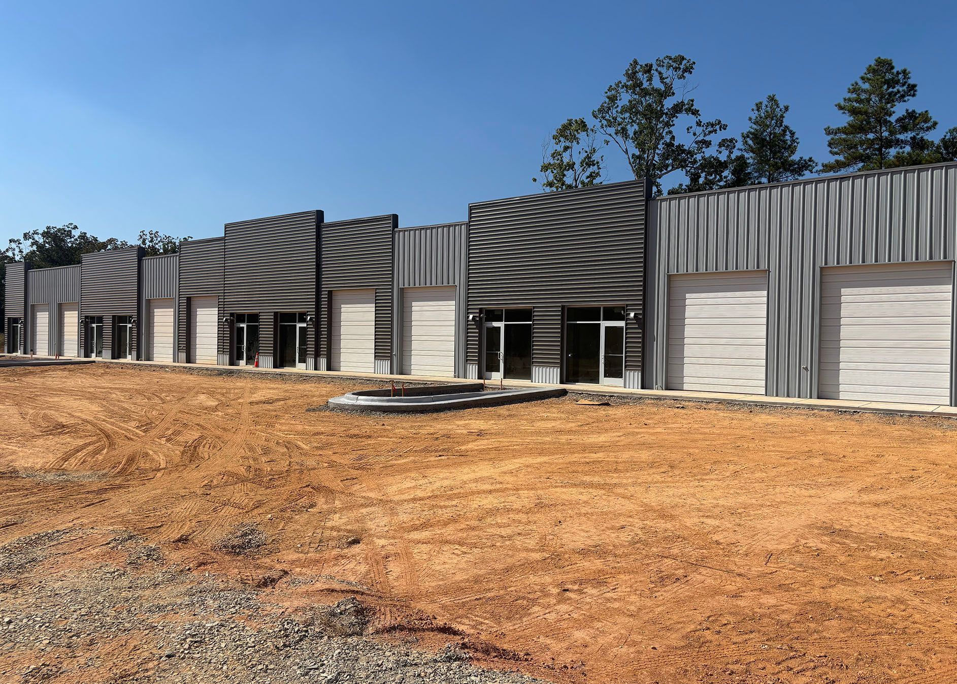 A row of new commercial buildings with corrugated metal siding on a dirt lot under a blue sky.