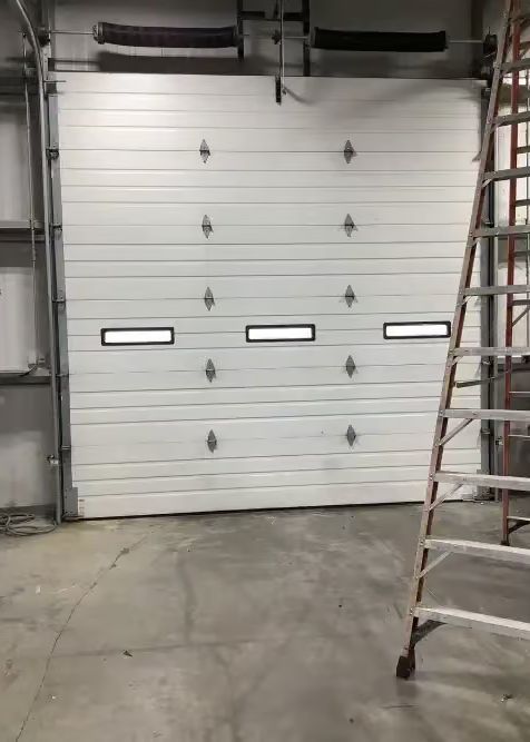 White commercial garage door, three windows, closed, with a ladder to the right.