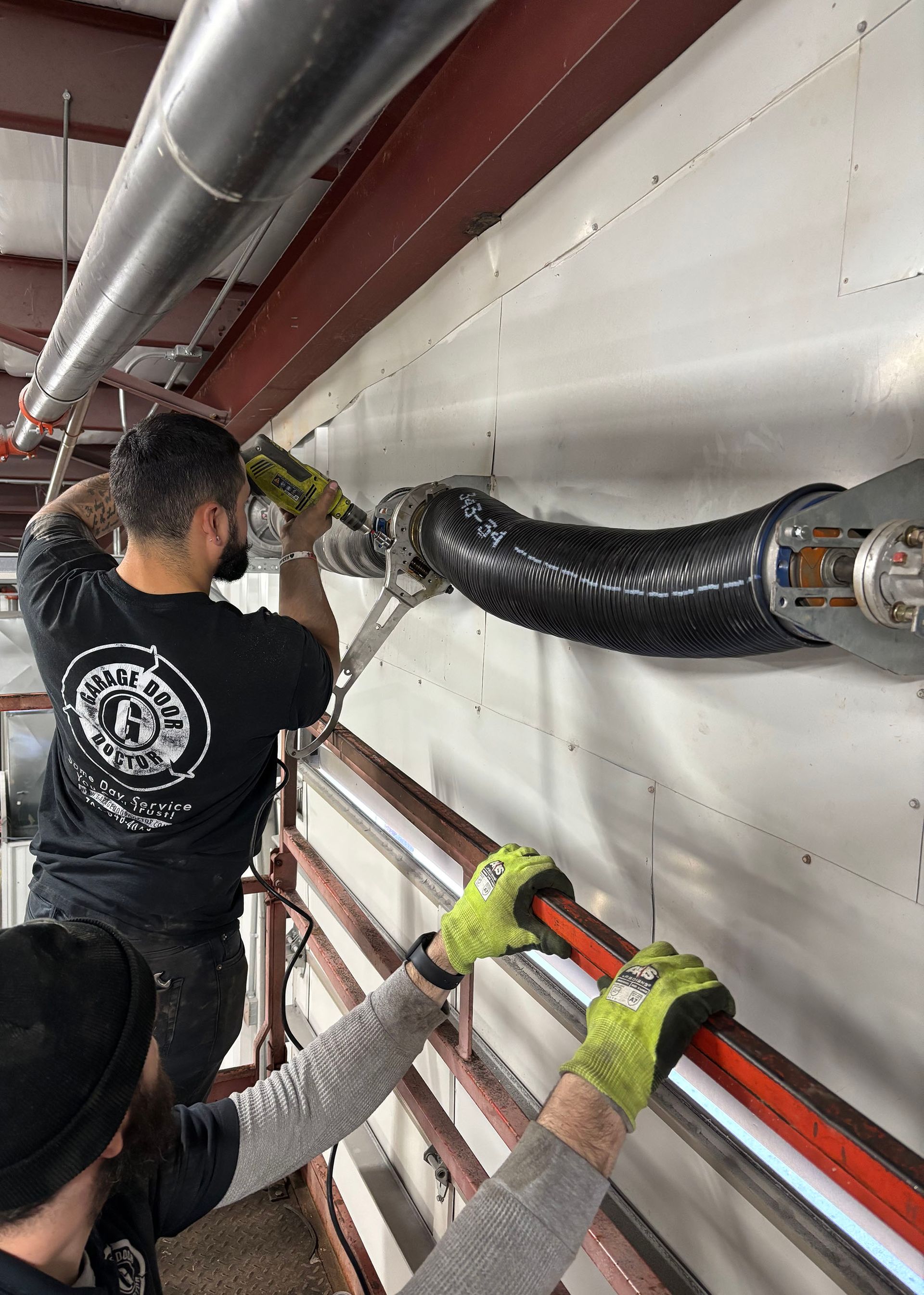 Two workers installing conduit on a wall. One uses sealant, the other holds the pipe.