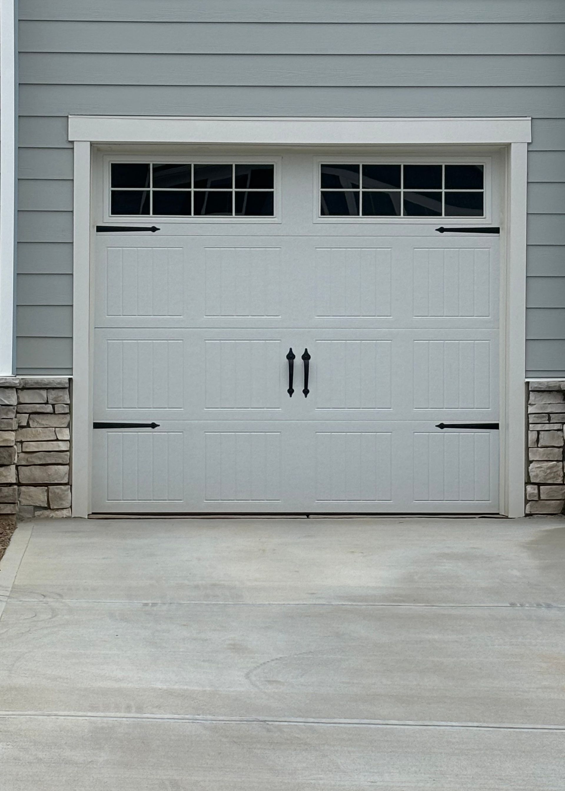 White garage door with windows and black hardware on gray siding.