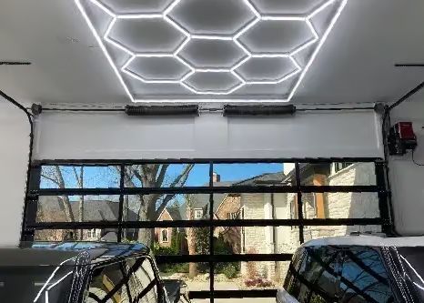 Garage interior with clear glass door open, showing neighborhood view; hexagonal ceiling lights.