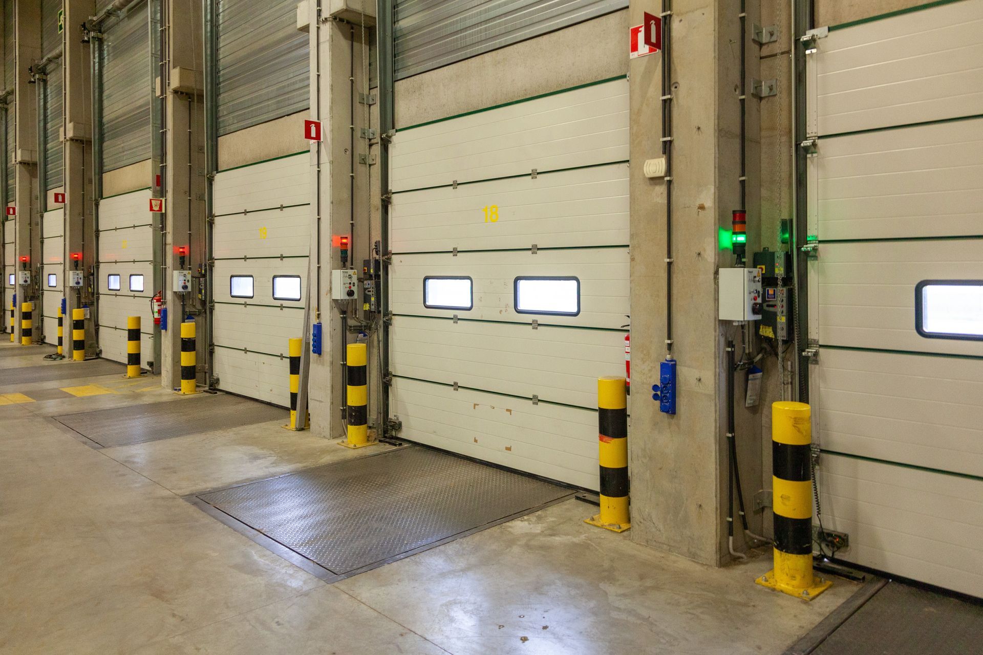 A series of warehouse loading dock doors with black and yellow bollards on a concrete floor.
