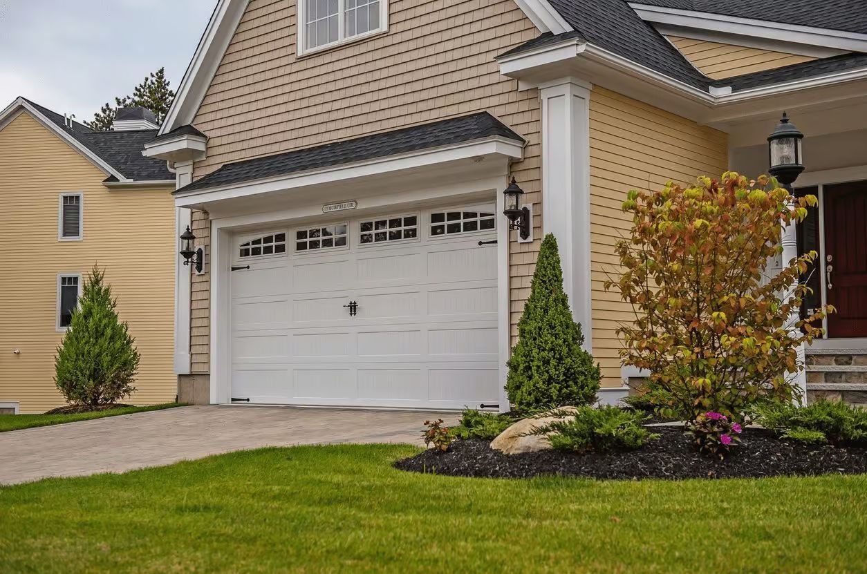 White garage door on a tan house with a driveway and landscaping; yellow house in the background.