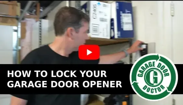Man locks a garage door opener. Black shirt, gray hair, indoors. White door and shelves visible.