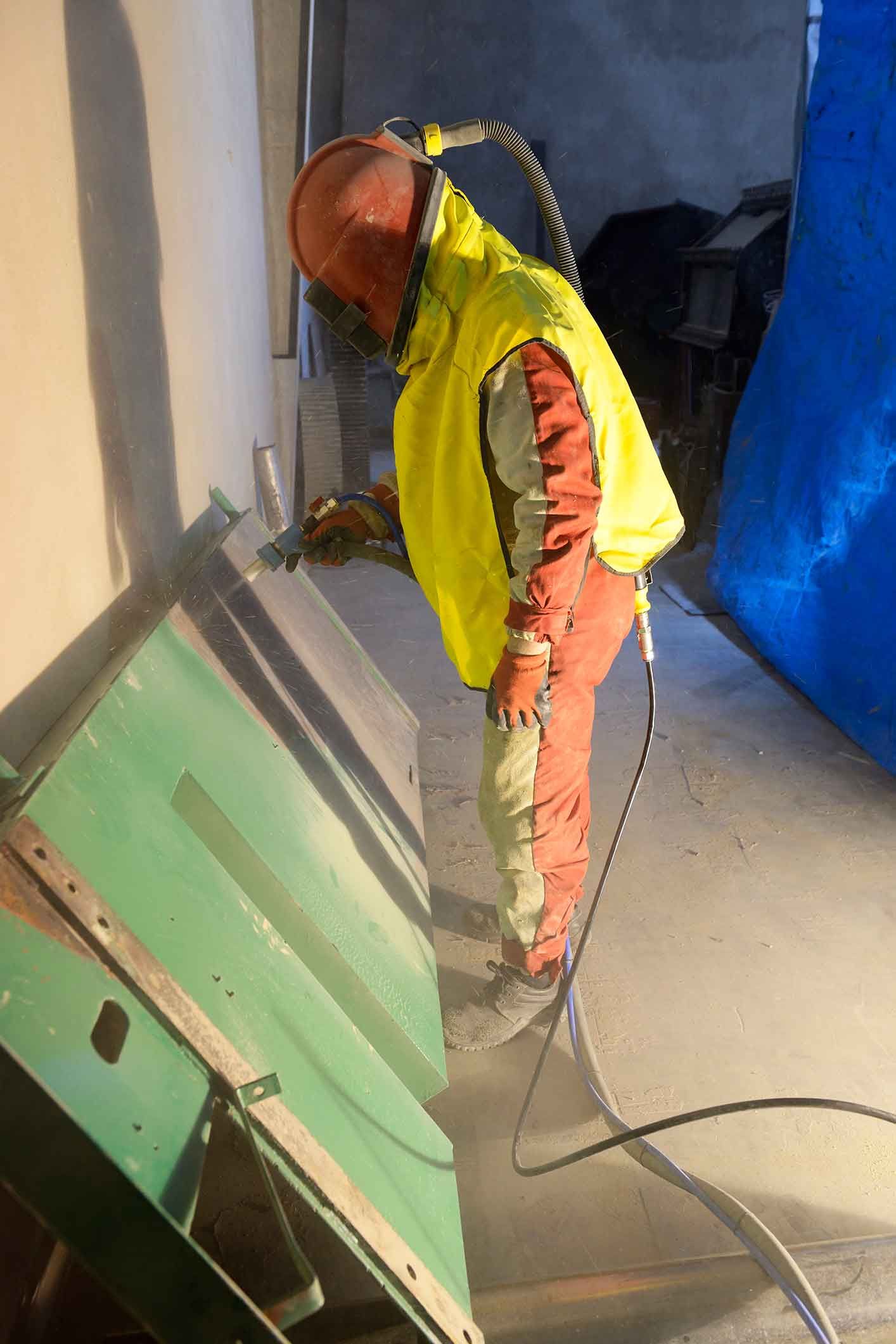 A man in a yellow vest is using a machine to sand a piece of metal.