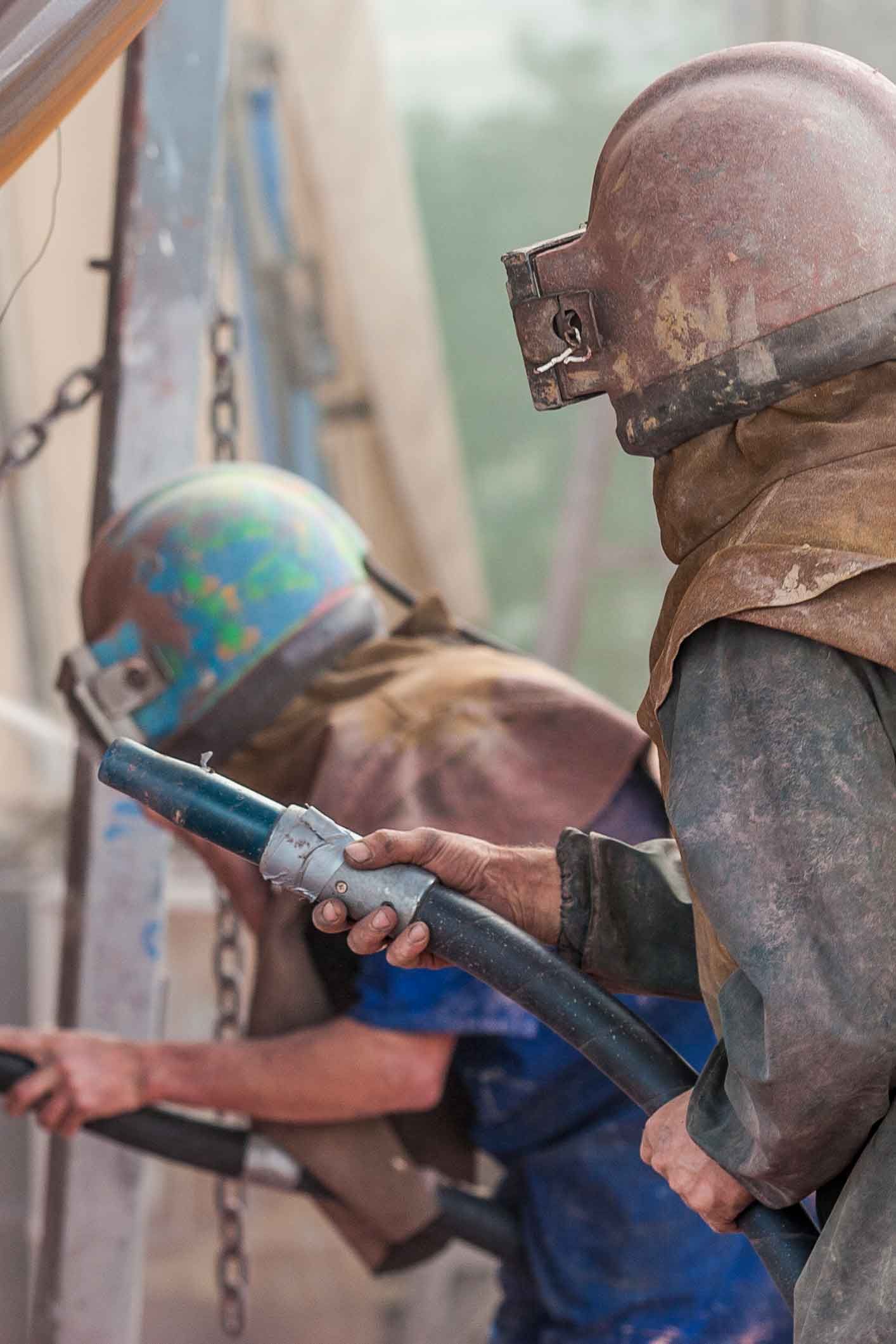 A worker sandblasting the corroded hull of a boat.