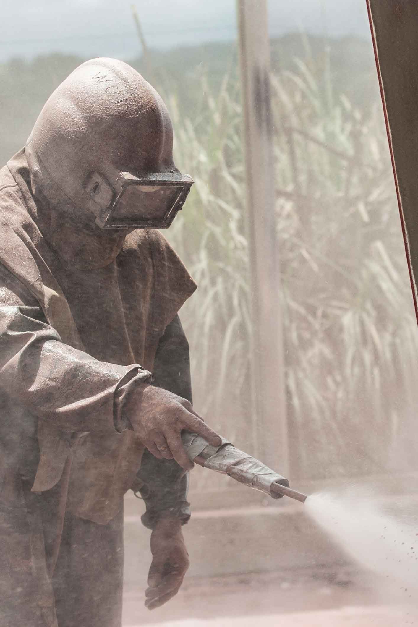 A man wearing a helmet and goggles is sandblasting a wall.