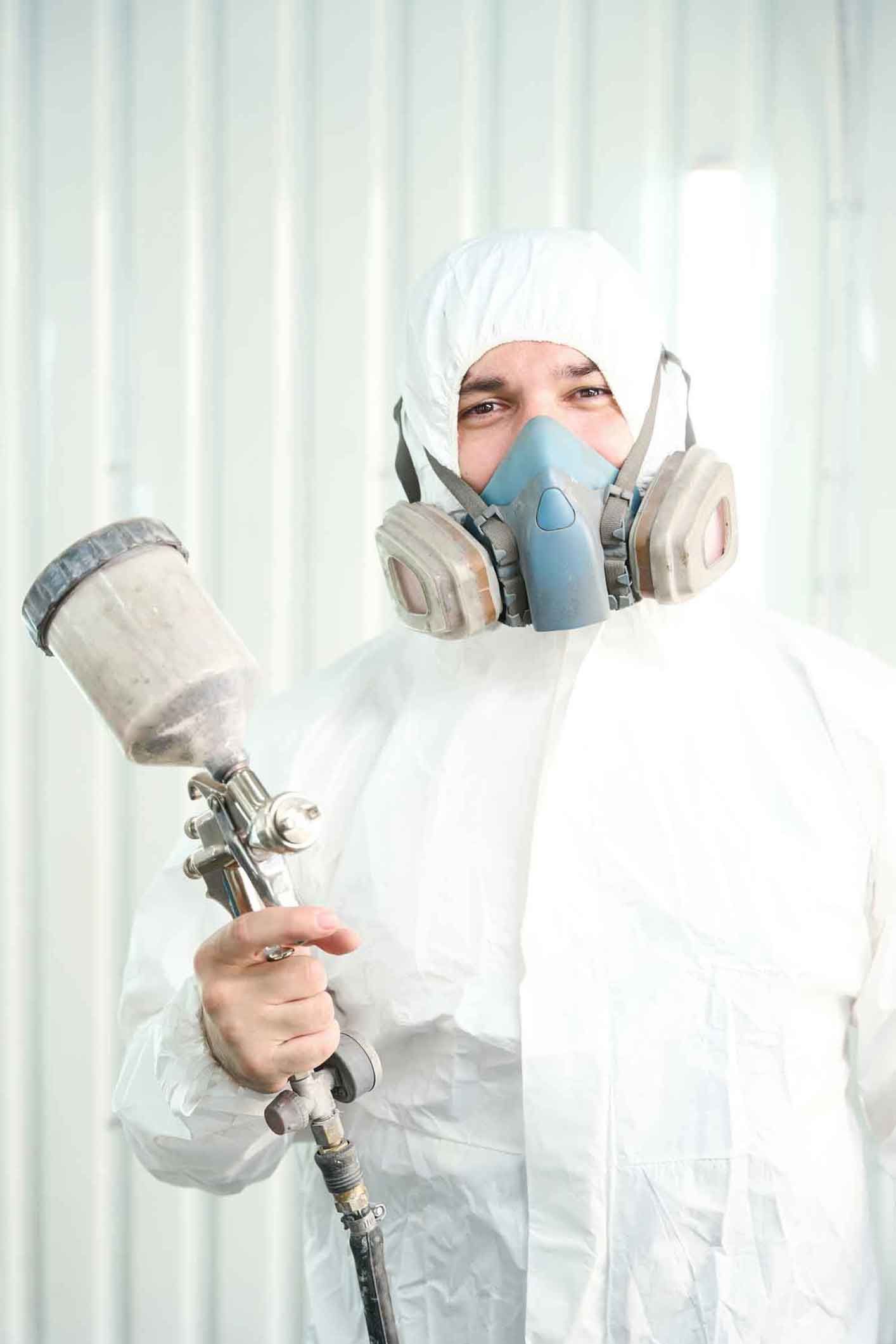 A man wearing a protective suit is holding a spray gun for painting.